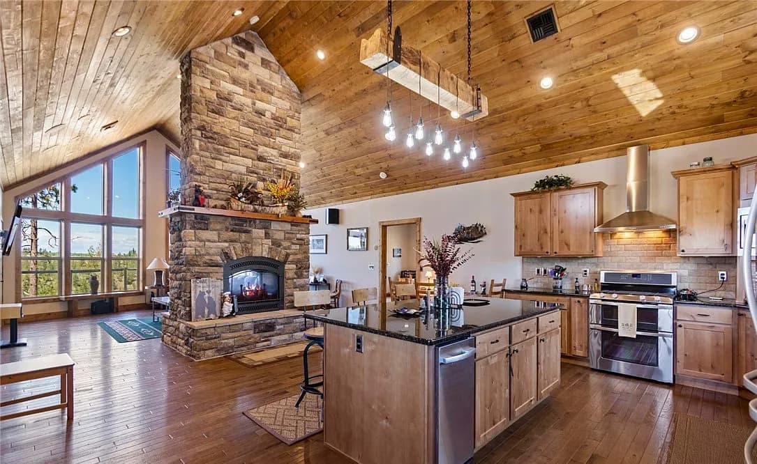 Open-concept great room with a floor-to-ceiling stacked-stone fireplace, vaulted wood ceiling, and gourmet kitchen