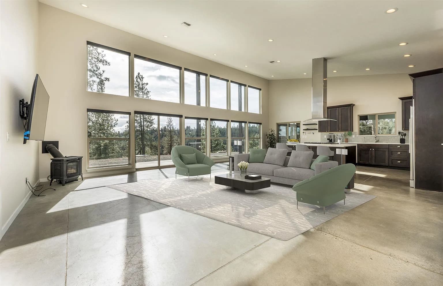 Open living room and kitchen with polished concrete floors and a wall of windows looking onto a pine forest