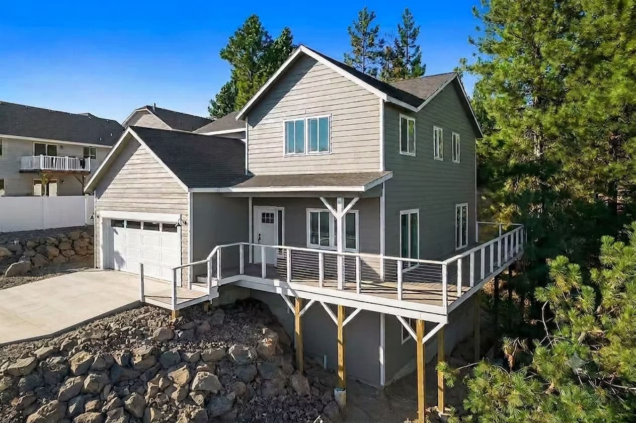 Two-story gray custom home with white trim, a walkout deck, and cable railings on a sloped lot