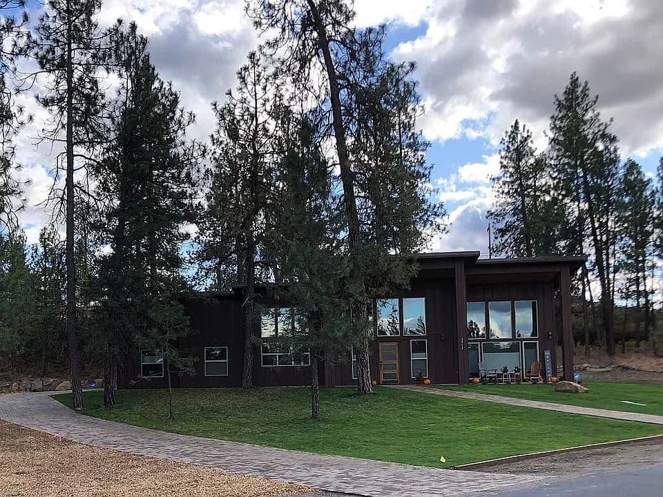 Dark modern custom home among pines with a wall of glass, a brick walk, and a deep roof overhang