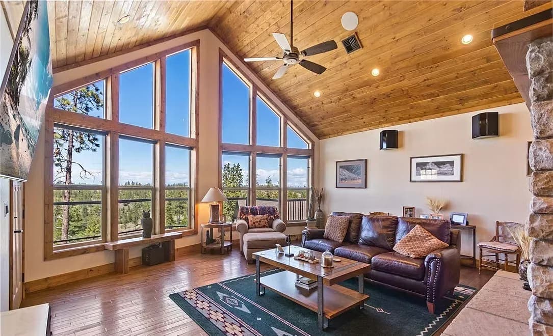 Vaulted living room with a two-story window wall, wood ceiling, and leather seating overlooking pines