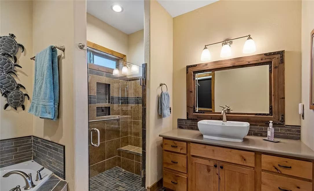 Bathroom with a glass walk-in shower, vessel sink, wood vanity, and tiled soaking tub surround