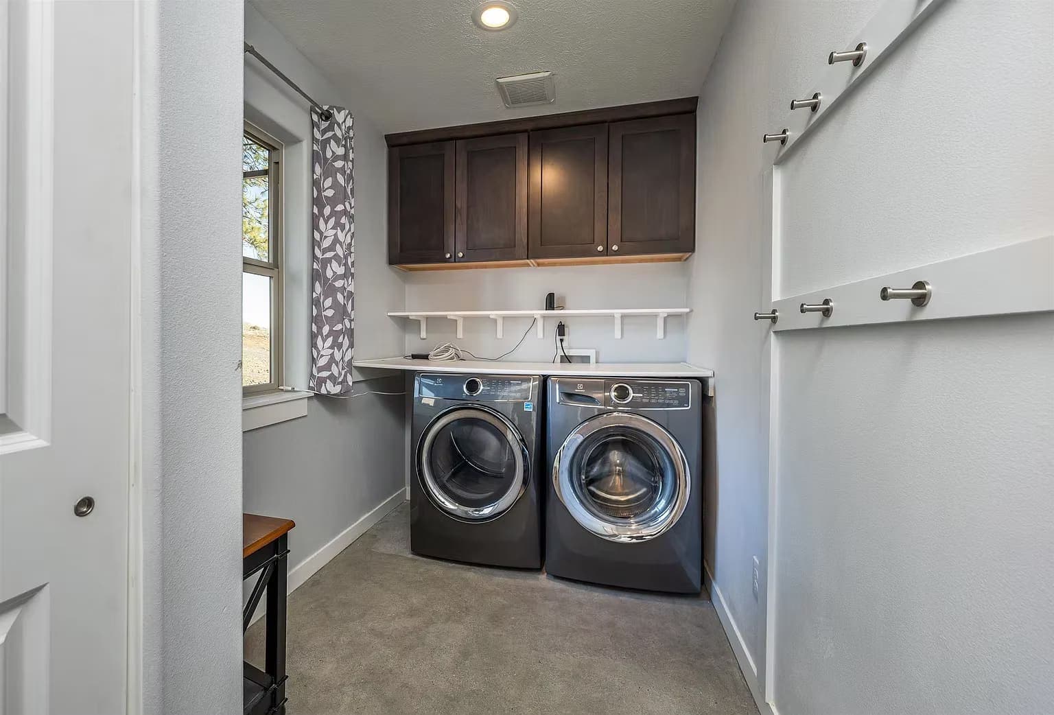 Laundry room with side-by-side stainless machines, dark cabinets, and a hanging rail
