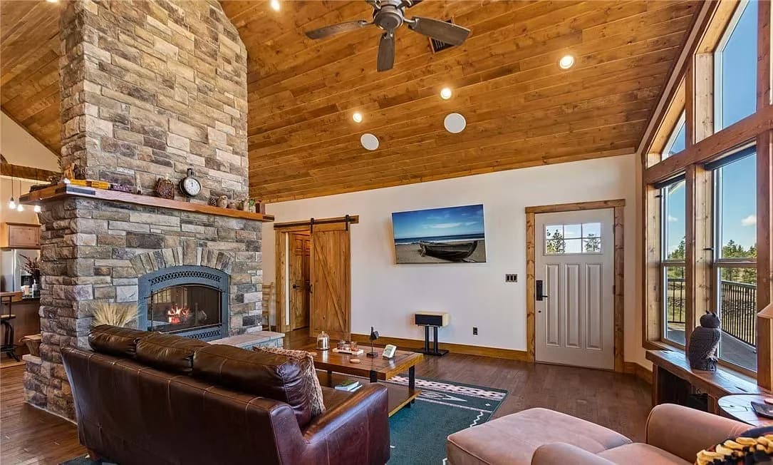 Living room with a stacked-stone fireplace, barn door, leather sofa, and vaulted wood ceiling