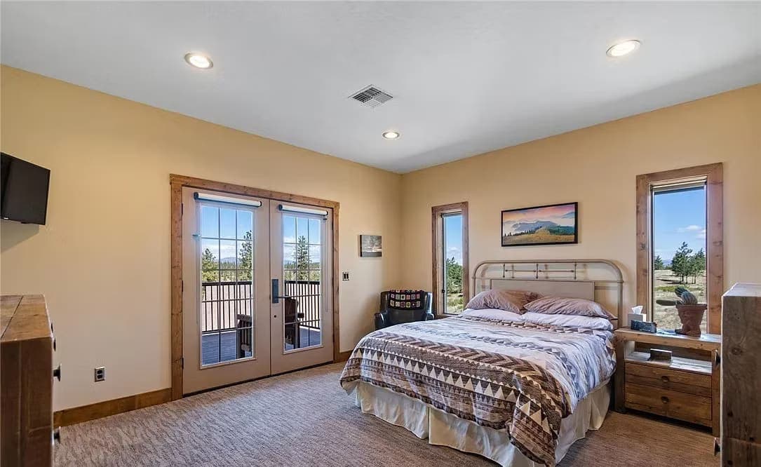 Bedroom with French doors to a deck, wood-trimmed windows, and views of the surrounding pines
