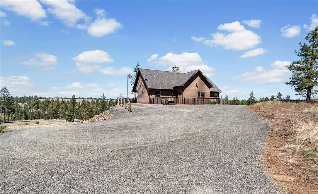 Custom home on a hilltop reached by a gravel drive, with pines and open country beyond