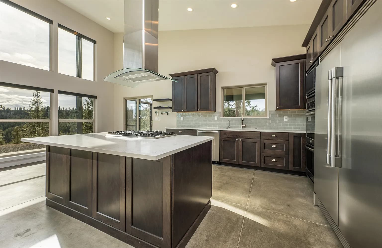 Custom kitchen with dark wood cabinetry, a large island cooktop, stainless appliances, and forest views