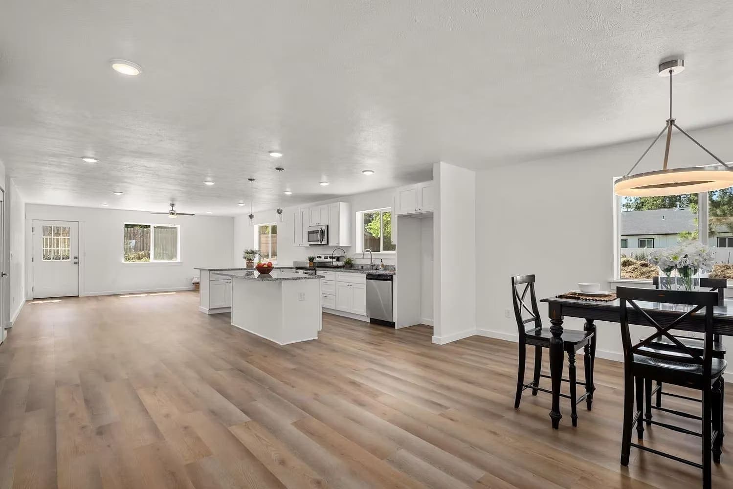 Open-plan living space with white kitchen, center island, dining table, and light wood floors
