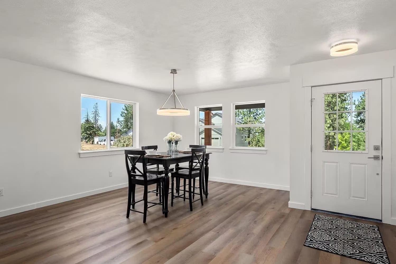 Dining room with a black table, wood floors, and a glass-lite entry door looking onto pines