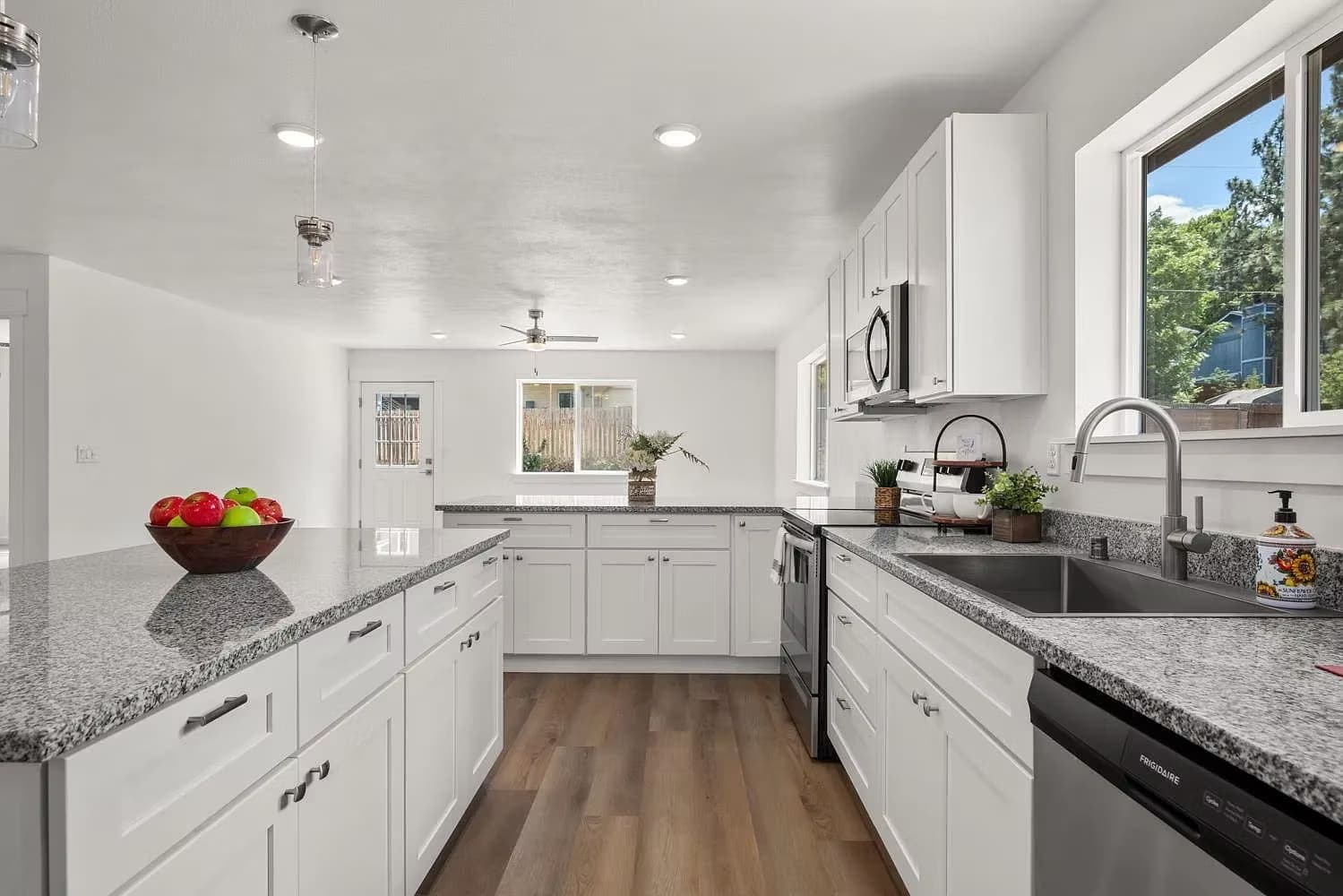 White galley kitchen with granite counters, stainless appliances, and a window over the sink