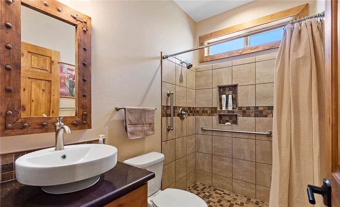 Guest bathroom with a vessel sink, tiled shower, and wood-framed mirror
