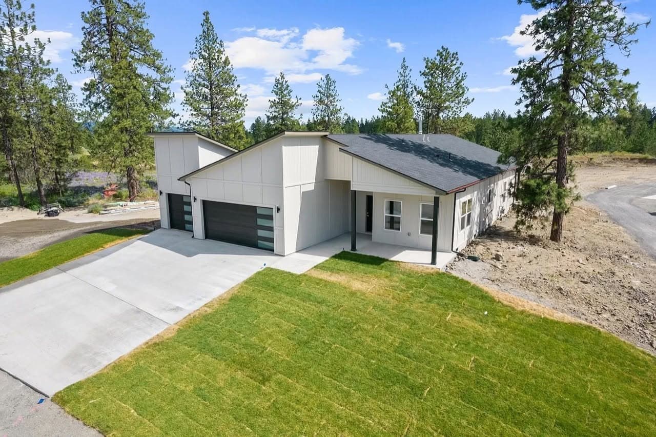 Newly completed modern home with white siding, black shed roofs, and a three-car garage